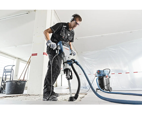 Ein Bauarbeiter benutzt einen Abbruchhammer mit Staubabsaugung in einem Raum.
