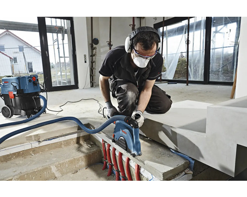 Ein Mann arbeitet mit einer Mauernutfräse und einem Staubsauger in einem Raum.