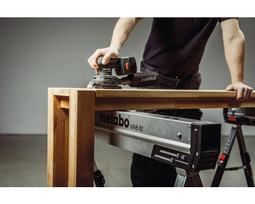 Ein Mann schleift Holz mit einem Metabo Exzenterschleifer auf einer Metabo MAB 82 Montagebank.