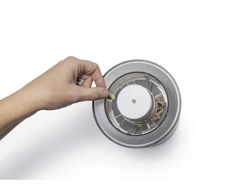 Eine Hand füllt einen Topf mit Saatgut ein.