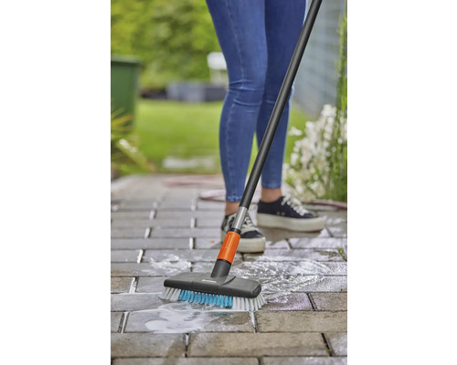 Person reinigt Pflastersteine mit einer Flächenbürste