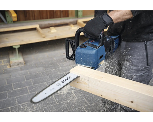 Eine Person sägt mit einer Akku-Kettensäge von Bosch ein Holzbrett.