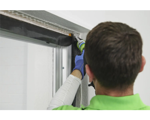 Ein Handwerker dichtet einen Fensterrahmen mit Dichtmasse ab.