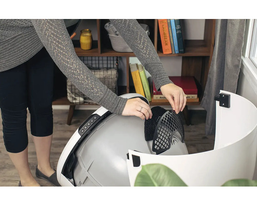 Eine Person setzt einen Filter in eine automatische Katzenstreu-Box ein.