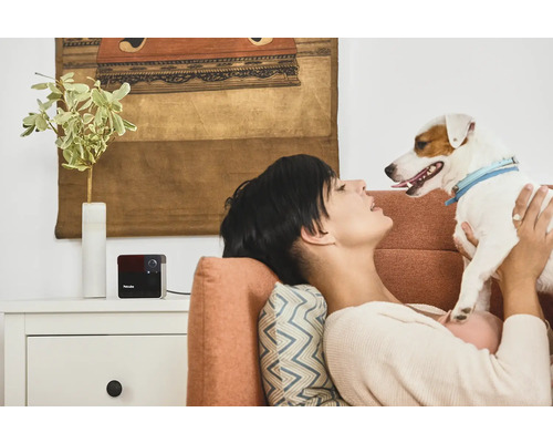 Frau entspannt sich mit Hund und Petcube Überwachungskamera auf dem Sofa