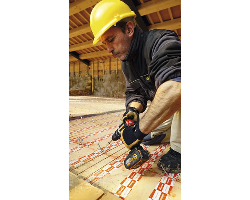 Handwerker mit Schutzhelm und Akkuschrauber bei der Installation von Dämmplatten auf einem Holzboden.