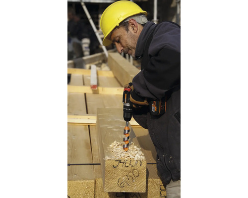 Ein Bauarbeiter bohrt mit einem Akkubohrer in einen Holzbalken.