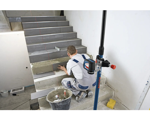 Handwerker verlegt Fliesen auf einer Treppe mit Hilfe eines Linienlasers