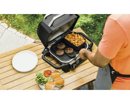 Elektrogrill mit Burgern, Pommes und Brötchen auf einem Holztisch