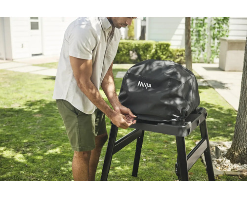 Mann befestigt eine Schutzhülle mit Ninja Logo an einem Grill