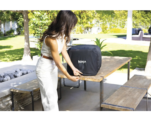 Eine Frau befestigt die Wetterschutzhülle von Ninja auf einem Grill im Freien.