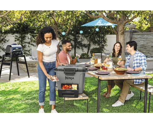 Szene im Garten mit Personen, einem Esstisch, einem Grill und einer Kühlbox der Marke Ninja