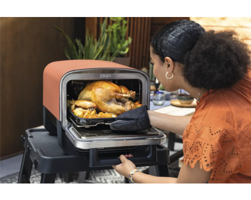 Frau öffnet den Ofen mit einem Brathähnchen