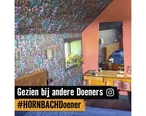 Schlafzimmer mit floral gemusterter Tapete an Wänden und Decke, Fenster, Spiegel und Kommode.