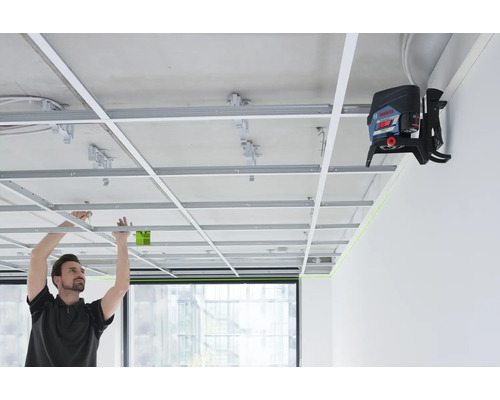 Ein Mann installiert eine abgehängte Decke mit einem Linienlaser zur präzisen Ausrichtung.