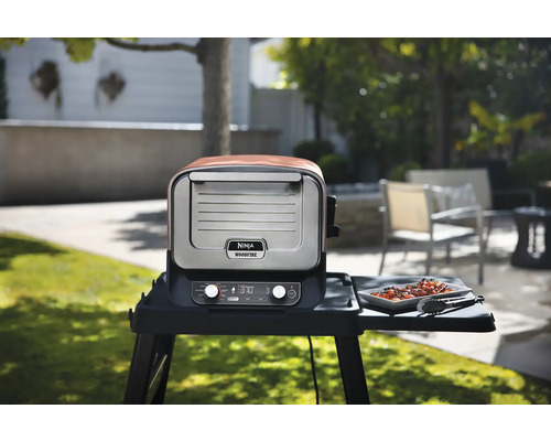 Ninja Woodfire Elektrogrill mit einem Gericht auf dem Seitentisch im Garten.