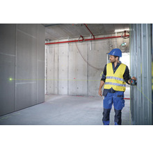 Ein Mann mit Helm und Sicherheitsweste verwendet einen Linienlaser in einem Rohbau, um die Ausrichtung zu prüfen.