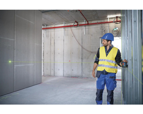 Ein Mann mit Helm und Sicherheitsweste verwendet einen Linienlaser in einem Rohbau, um die Ausrichtung zu prüfen.
