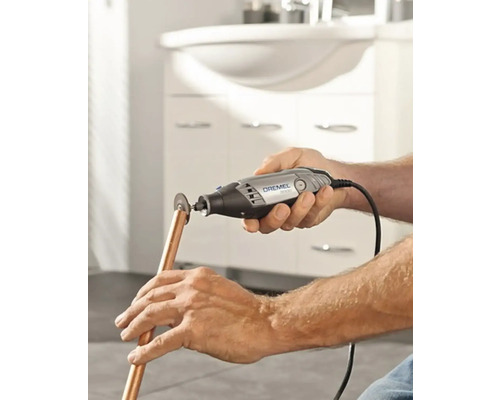 Eine Person schneidet mit einem Dremel Multifunktionswerkzeug ein Kupferrohr.