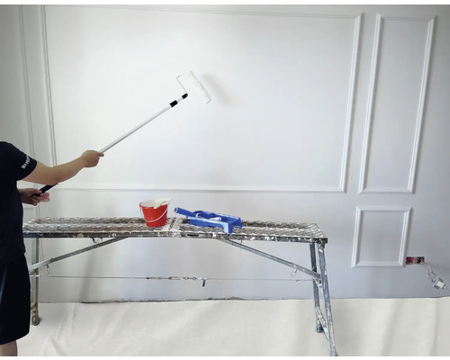 Maler streicht mit Farbroller und Teleskopstiel eine weiße Wand von einem Gerüst aus.