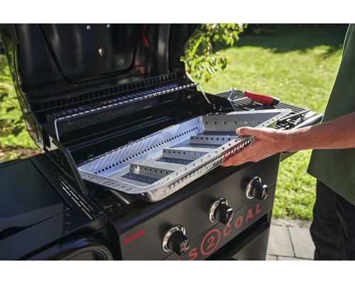 Ein Mann setzt eine Grillkohleschale in einen Gasgrill für Holzkohle