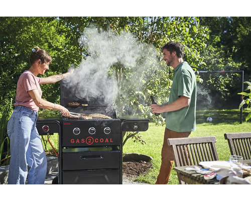 Frau und Mann grillen mit einem Gas- und Kohlegrill im Garten.