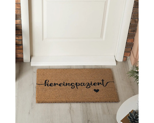 Fußmatte aus Kokosfaser mit der Aufschrift ''hereinspaziert'' und einem Herzsymbol vor einer Tür