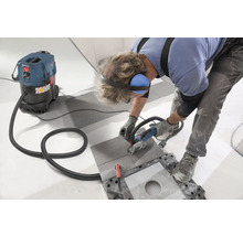 Handwerker schneidet Fliese mit einem Trennschleifer, während ein Industriestaubsauger Staub absaugt.