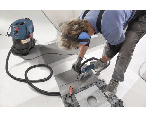 Handwerker schneidet Fliese mit einem Trennschleifer, während ein Industriestaubsauger Staub absaugt.