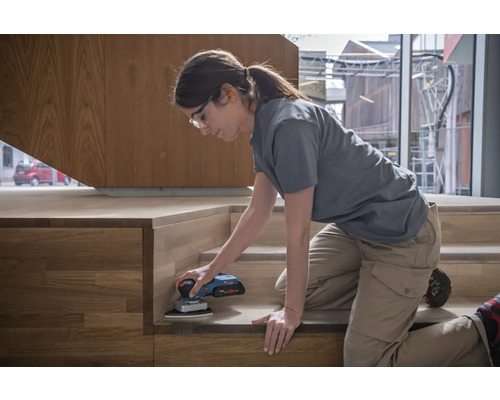 Frau schleift Holztreppe mit einem Schleifgerät