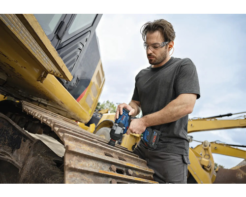 Ein Mann mit Schutzbrille arbeitet mit einem Akku-Schlagschrauber an einer Baumaschine.