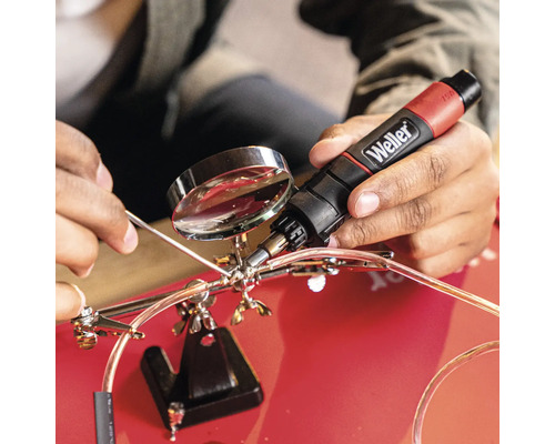 Person lötet mit einem Weller Lötkolben und einer Dritter-Hand-Lupe