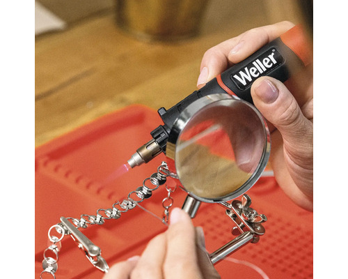 Eine Hand hält einen Weller Lötkolben beim Löten einer Kette mit einer Lupe