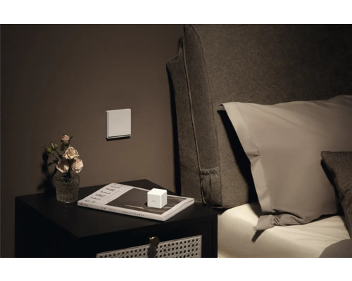 Nachttisch mit Dekoration, Schalter an der Wand und Bett im Hintergrund