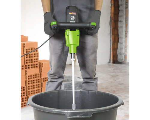 Ein Mann benutzt einen Mörtelrührer in einem Eimer auf einer Baustelle.