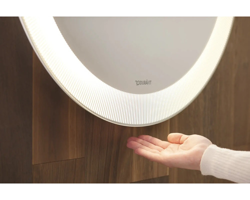 Beleuchteter Duravit Spiegel mit Hand vor Holzwand