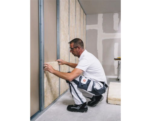 Ein Mann montiert Dämmmaterial zwischen Metallprofilen an einer Wand.