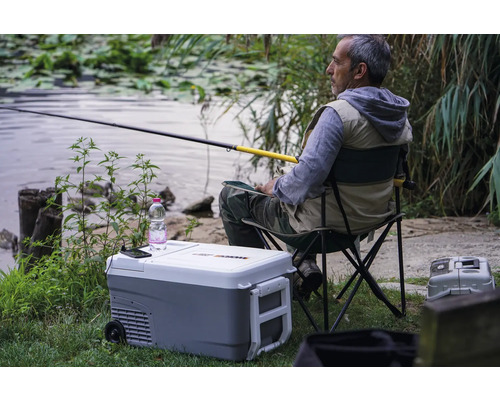 Angler sitzt mit Angel neben einer Kühlbox am See
