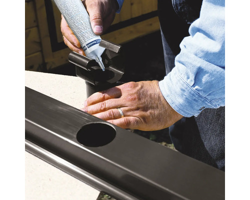 Person trägt Dichtstoff auf ein Fallrohr für die Regenrinne auf