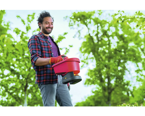 Ein Mann benutzt einen Düngerstreuer im Garten.