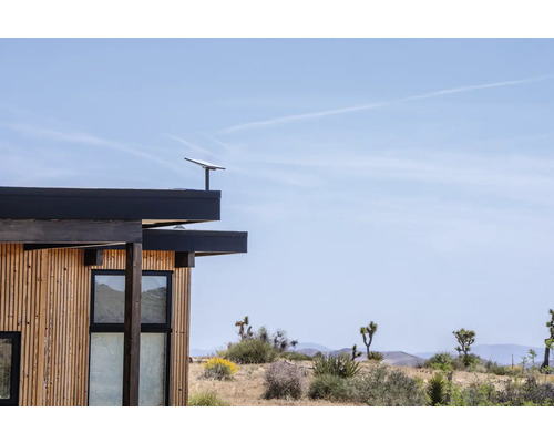 Hausfassade mit Holzverkleidung, Fenstern und Solaranlage auf dem Dach.