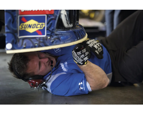 Ein Mechaniker liegt unter einem Fahrzeug, das mit dem Sunoco Logo versehen ist, und führt Wartungsarbeiten durch