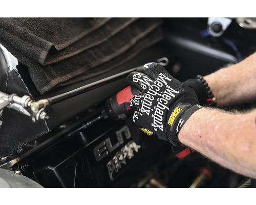 Eine Person arbeitet mit einem Schraubendreher an einem Fahrzeug. Arbeitskleidung wird verwendet.