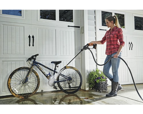Frau reinigt ein Fahrrad mit einem Hochdruckreiniger vor einer Garage.