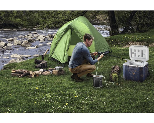 Szene einer Campingausrüstung mit Zelt, Kühlbox, Feuerholz und Person bei der Reinigung