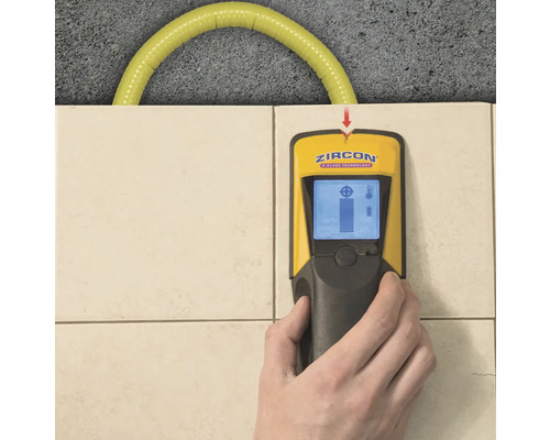 Eine Hand hält einen gelb-schwarzen Leitungssucher an einer gefliesten Wand