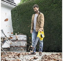 Mann benutzt einen Laubbläser im Garten, um Blätter zu entfernen.