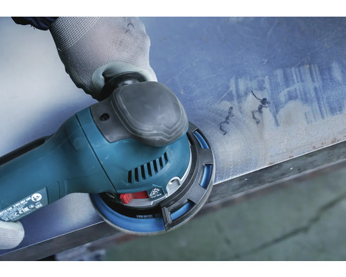 Eine Hand mit Handschuh bedient einen Exzenterschleifer auf einer Metalloberfläche.