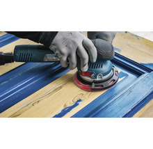 Ein Handwerker schleift mit einem Exzenterschleifer eine blaue Holztür.