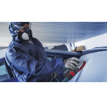Eine Person in Schutzkleidung schleift ein Auto mit einem Schleifgerät.